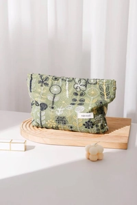 Detail of floral embroidery on a linen makeup bag with lifestyle props on wood
