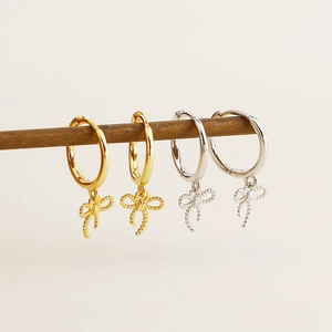 Detailed close-up of S925 silver bow earrings in gold and silver finishes on a wood stand