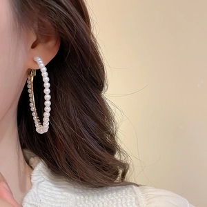 Close-up of elegant gold hoop earrings with white pearls on a model with brown hair