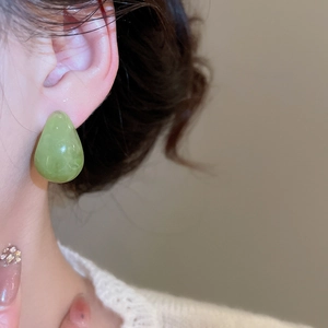 Close-up of elegant green resin teardrop earrings worn by a model in a cozy knit sweater
