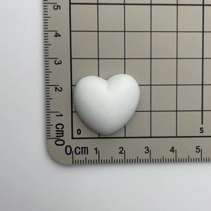 Macro shot of 3cm white heart resin charm with Sweet engraving on a grid measuring mat
