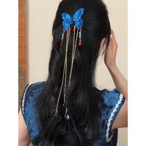 Détail de la pince à cheveux papillon brodée bleue avec chaînes à pompons dorés