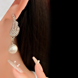 Close-up of sparkling wing earrings with white pearl detail on a model's ear