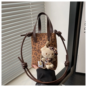 Detailed close-up of leopard print canvas bag with brown leather handles and plush charm
