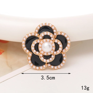 Détail de l'accessoire camélia en alliage avec perles blanches et émail noir poli