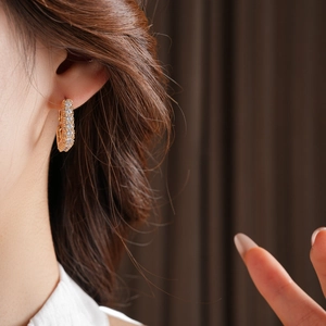 Détail d'une boucle d'oreille en U dorée avec zircons brillants portée par un modèle