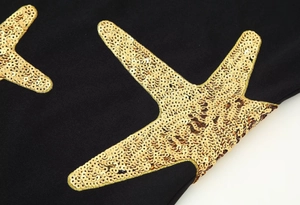 Detailed view of golden sequin starfish embroidery on black fabric dress