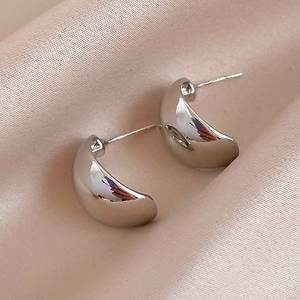 Polished silver geometric curved stud earrings on elegant champagne silk background