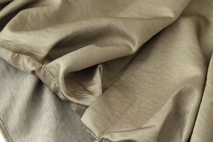 Close-up of champagne gold satin fabric texture and premium stitching on bomber jacket