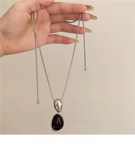 Detail of silver snake chain necklace with black oval resin pendant and teardrop metal piece