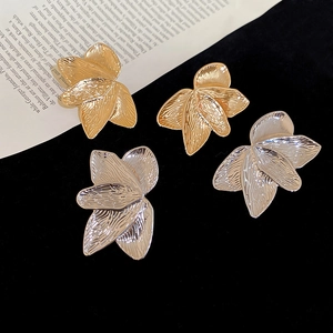 Detailed close-up of textured gold and silver leaf earrings on black velvet background