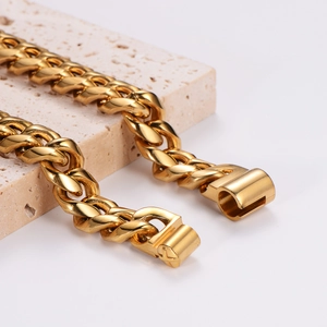 Men's chunky gold Cuban link chain necklace in stainless steel on a textured stone base