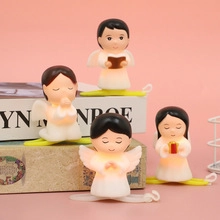 Détail de quatre veilleuses anges blancs avec socles jaunes sur fond rose tendre