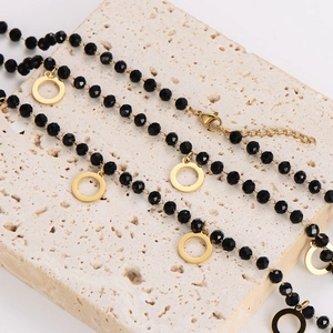 Minimalist necklace with black glass beads and gold circle pendant on beige stone