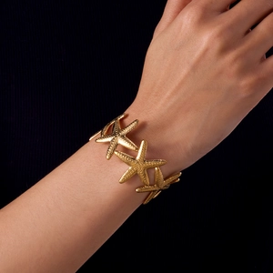 Close-up of golden starfish bracelet with textured relief on female model's wrist