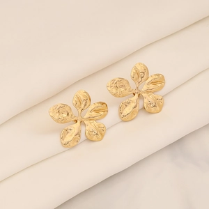 Detailansicht goldener Blumenohrringe mit Hammerschlag-Struktur auf beigem Seidenstoff