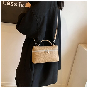 Detail view of khaki lychee leather handbag with silver zipper and top handle on a model