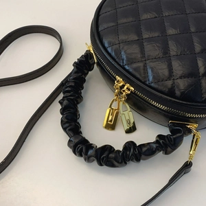 Close-up detail of black quilted round bag with ruched handle and gold lock zipper pulls.