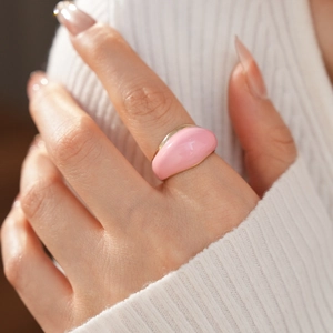Close-up of a pink enamel gold ring on a finger with a cozy white knit sweater background