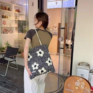 Vue extérieure d'un grand sac cabas noir à fleurs blanches avec bandoulière verte