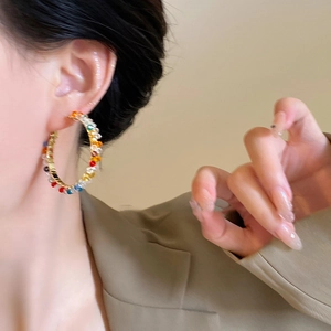 Colorful beaded gold hoop earrings with faceted crystals worn by a model in a close-up shot