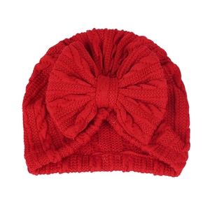 Détail d'un turban rouge tricoté pour bébé avec motif torsadé et un grand nœud