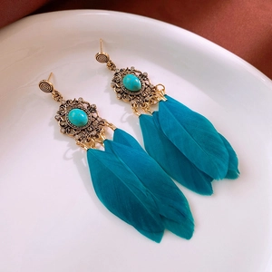 Détail des boucles d'oreilles dorées vintage avec plumes sarcelle et pierre sur plat céramique
