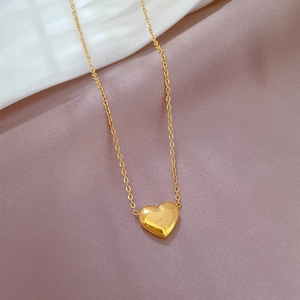 Gros plan d'un pendentif cœur doré sur chaîne en O, sur satin rose et fond blanc