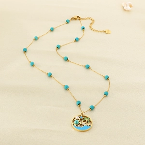 Collier de plage doré avec pendentifs palmier et tortue sur un fond de sable fin