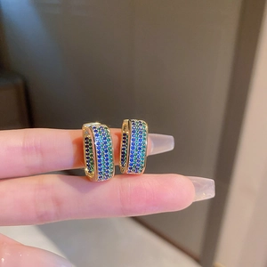 Close-up of geometric gold earrings featuring pavé-set blue and green crystals