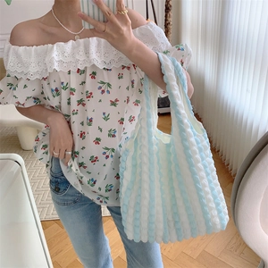 Detail of blue and white striped bubble texture tote bag held by a model in a bright room