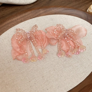 Detailed close-up of pink satin bow earrings with glass bead flower tassels on wood