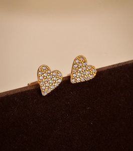 Detailed view of gold S925 heart earrings with micro-set cubic zirconia on velvet stand