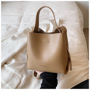 Detail view of a light brown leather bucket bag with gold MACGHEE branding and handle