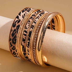 Dettaglio di 10 braccialetti dorati con stampa leopardata sovrapposti su un supporto