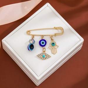 Detail of gold evil eye brooch with tassel charms on a white jewelry cushion