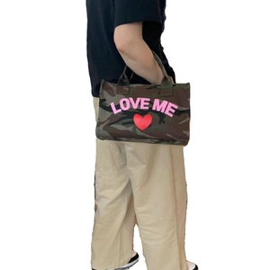 Camo canvas tote bag with pink Love Me text and red heart shown on a female model