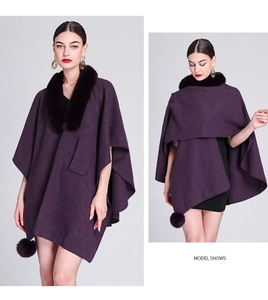 Detail of dark purple knitted cloak with a plush faux fur collar and pom-pom tassels