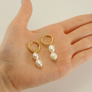 Detail of hand holding 18k gold earrings with natural baroque twin pearls