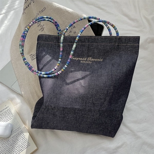 Close-up detail of vintage denim tote bag with colorful beaded straps and gold logo