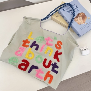 Detail of colorful chenille embroidery on a grey canvas tote bag with woven handles