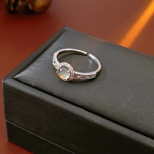Macro shot of silver ring with pale green gemstone and pavé diamonds on textured band