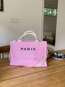Close-up of pink straw tote bag with black PARIS embroidery on a wooden table