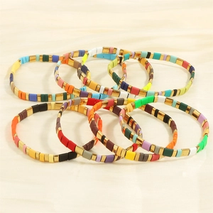 Close-up of seven colorful Tila bead bracelets with gold accents on silk background