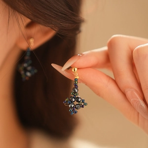 Close-up of diamond-shaped floral beaded earrings in iridescent dark finish