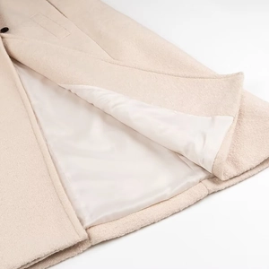 Dettaglio del cappotto di lana beige che mostra il tessuto strutturato e la fodera liscia