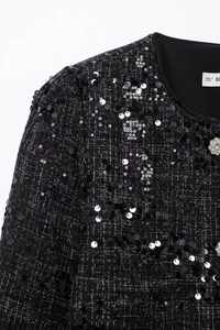 Nahaufnahme einer schwarzen Tweed-Jacke mit funkelnden Pailletten und Silberknöpfen