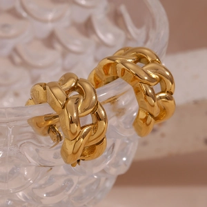Detailed view of gold Cuban chain hoop earrings hanging on a wavy glass bowl edge