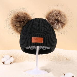 Detail of black winter cable knit baby hat with dual pom-poms and leather brand label