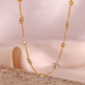 Detailed close-up of golden chain necklace with floral zircons on soft silk background